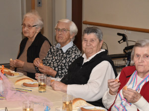 Vier ältere Frauen sitzen gemeinsam am Tisch, essen Würstel mit Brot und genießen die Feierlichkeiten. 