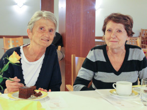 Angehörige und Bewohnerin sitzend nebeneinander im Gegenrationensaal des ÖJAB-Hauses Neumargareten.