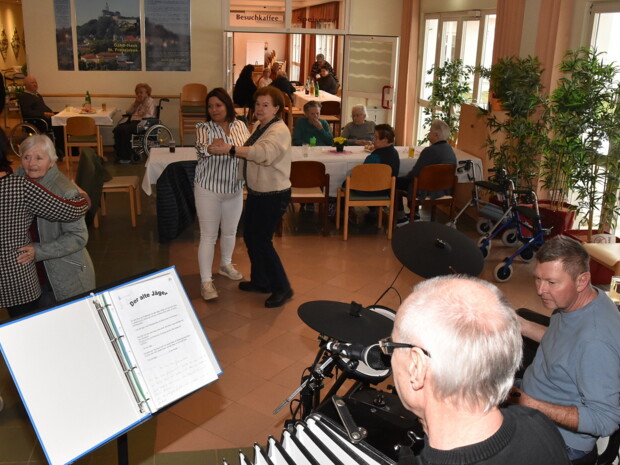 In der Eingangshalle tanzen mehrere Personen zu Live-Musik, gespielt von zwei Musikern mit Akkordeon und Schlagzeug. Andere Gäste sitzen an den Tischen und schauen zu.
