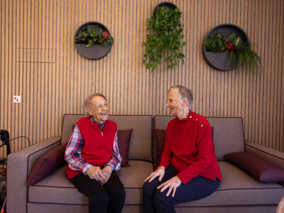 Zwei Bewohner:innen sitzen auf einem Sofa im Gemeinschaftsraum und unterhalten sich fröhlich. Foto: ÖJAB / Erika Mayer.