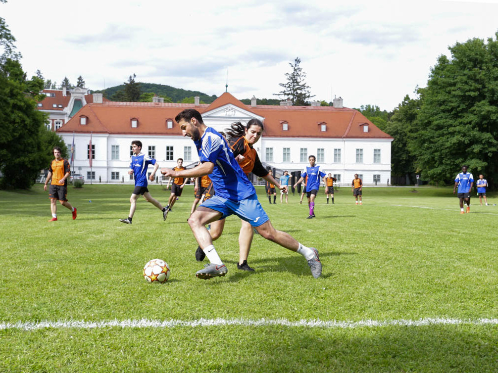 Spiieler:innen im Zweikampf um den Ball auf der Grünflache, im Hintergrund das barocke Schloss Miller-Aichholz.